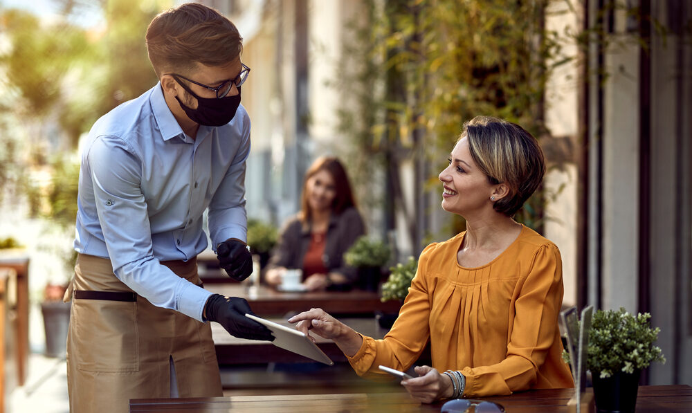 Waiter serving woman outdoors with mask